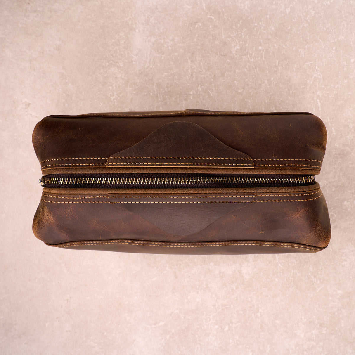 The Grafton leather toiletry bag closed, shot top down, showing the brass zip and leather grain