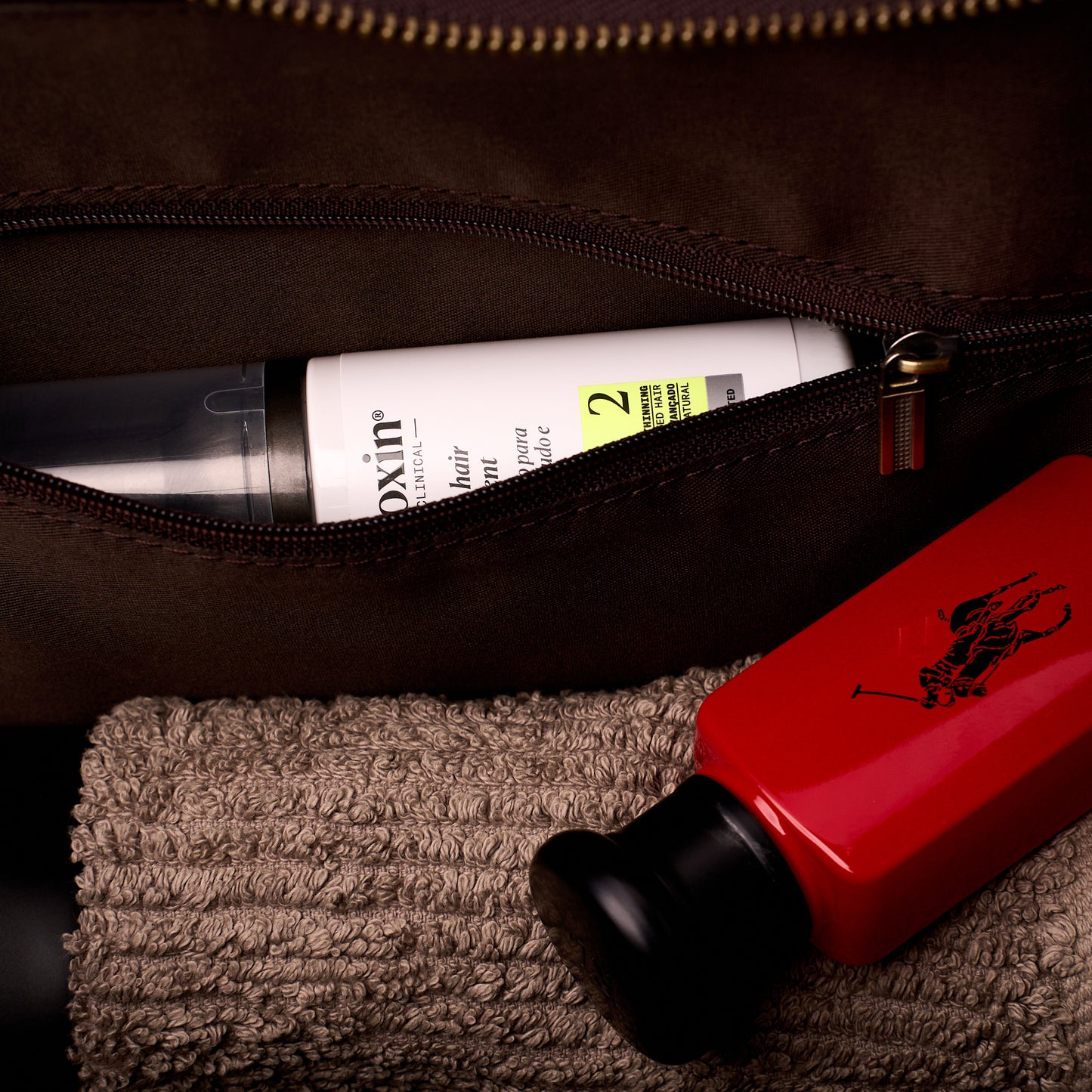 A bottle being tucked into the zipped inner pocket of The Grafton leather toiletry bag