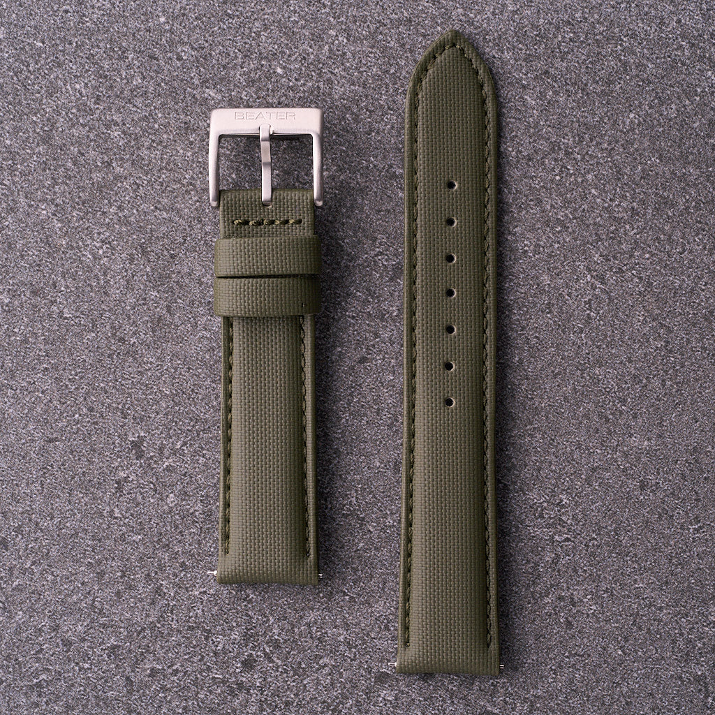 A green waterproof watch strap with a silver buckle laid out flat on a textured grey surface.