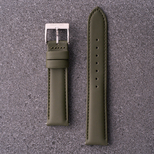 A green waterproof watch strap with a silver buckle laid out flat on a textured grey surface.