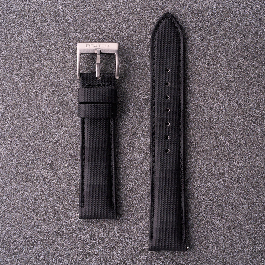 A black waterproof watch strap with a silver buckle laid out flat on a textured grey background.