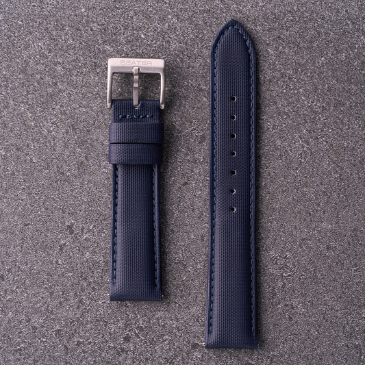 A navy blue waterproof watch strap with a silver buckle laid out flat on a textured grey surface.