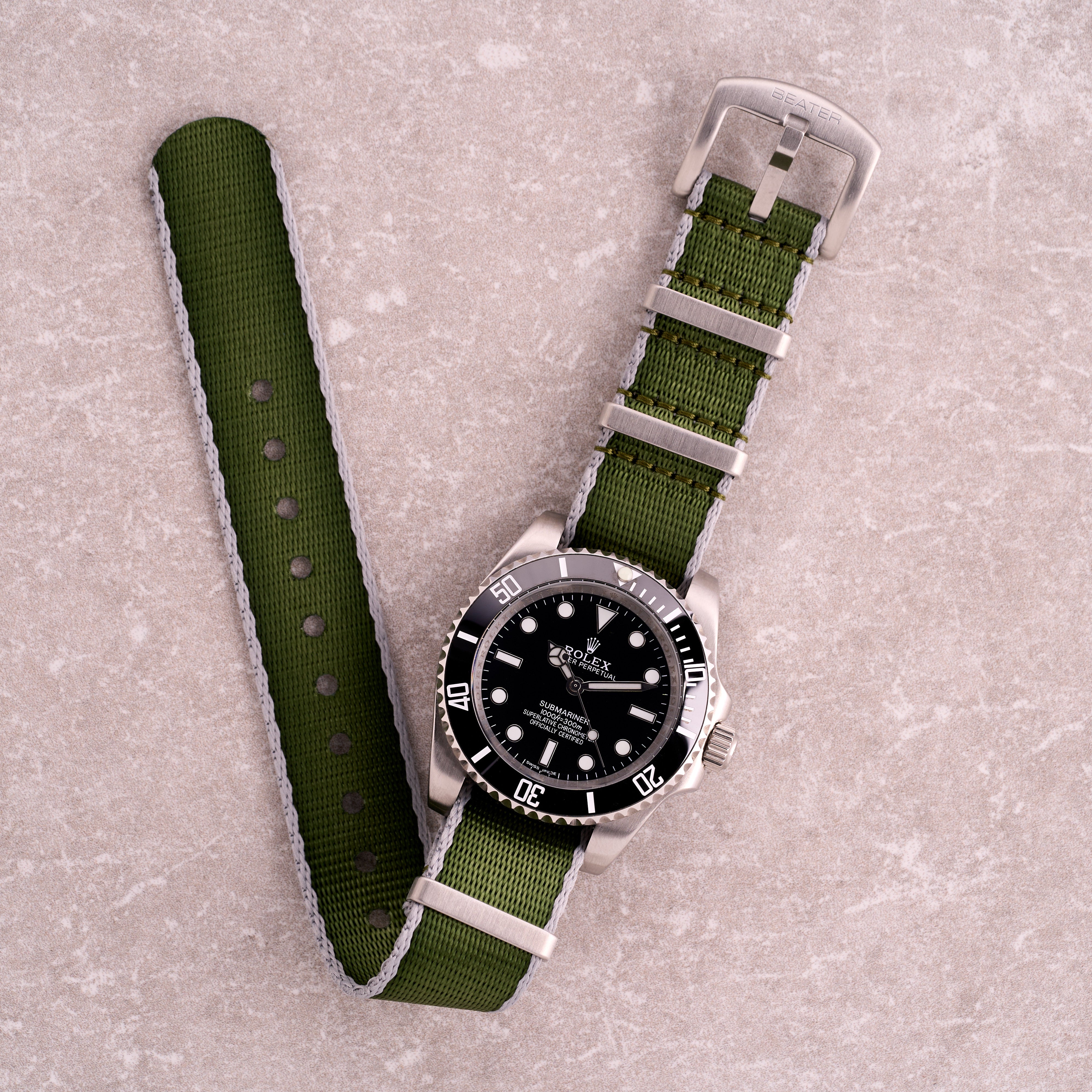 The Sentinel green with grey edge seatbelt NATO strap, dark green nylon one-piece watch strap with contrasting grey borders and steel hardware.